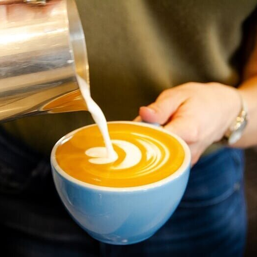 Barista pouring textured milk into a flat white to form latte art